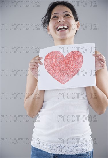 Young woman holding a piece of paper with a heart drawn on it