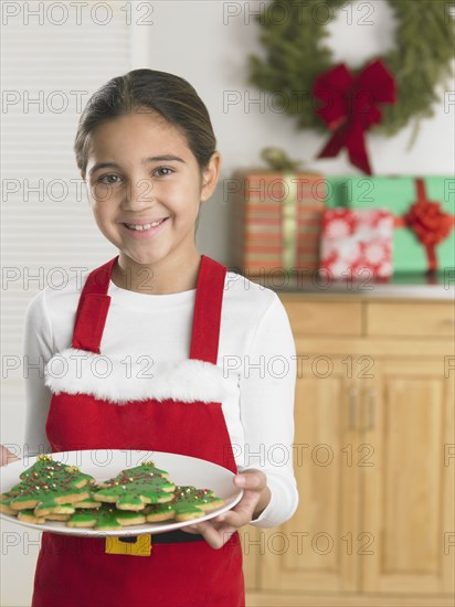 Young girl in a Santa apron holding a plate of Christmas cookies