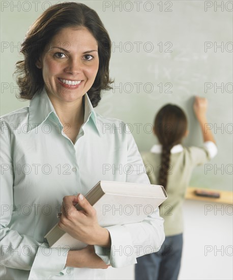 Teacher smiling for the camera as student works in the background