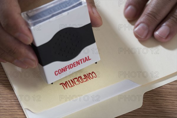 Close up of male hands using confidential stamp on file