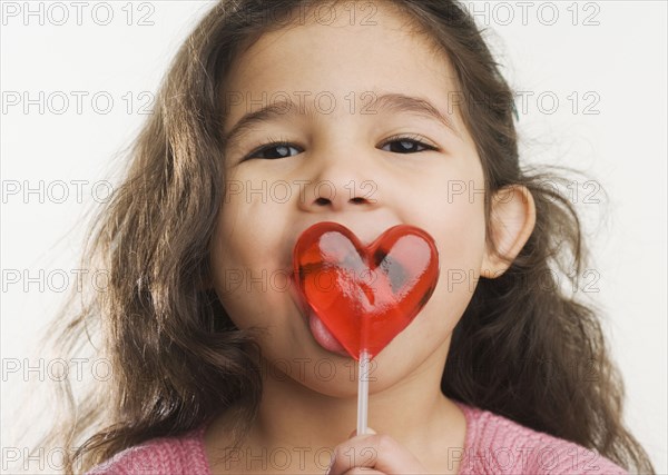 Studio shot of Hispanic girl licking heart lollipop