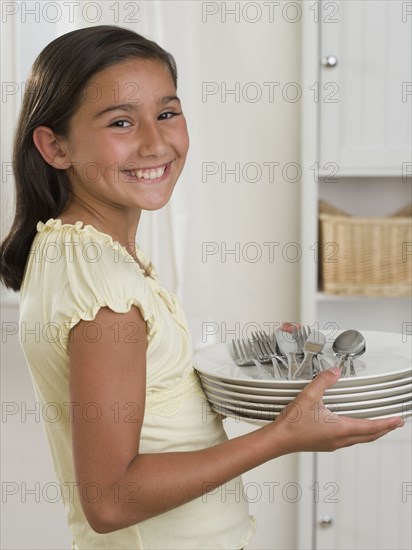 Hispanic girl smiling with stack of plates and silverware