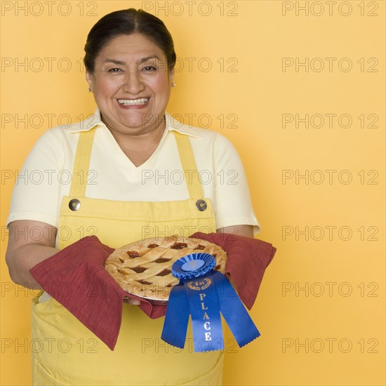 Senior Hispanic woman holding pie with first place ribbon