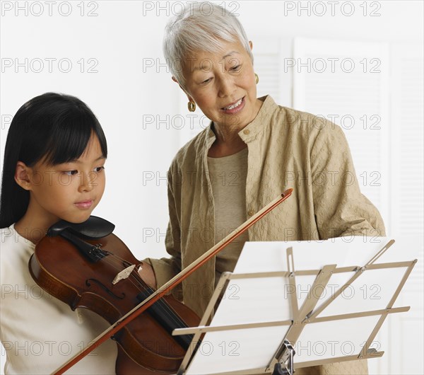Senior Asian woman teaching young Asian girl violin