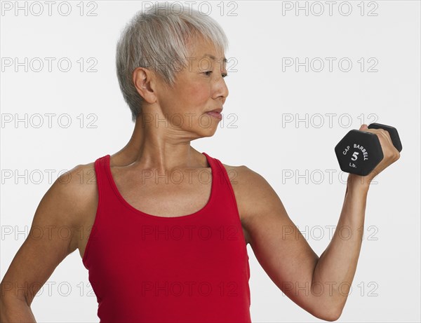 Studio shot of senior Asian woman lifting dumbbell