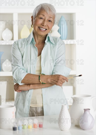 Senior Asian woman smiling with pottery and paints