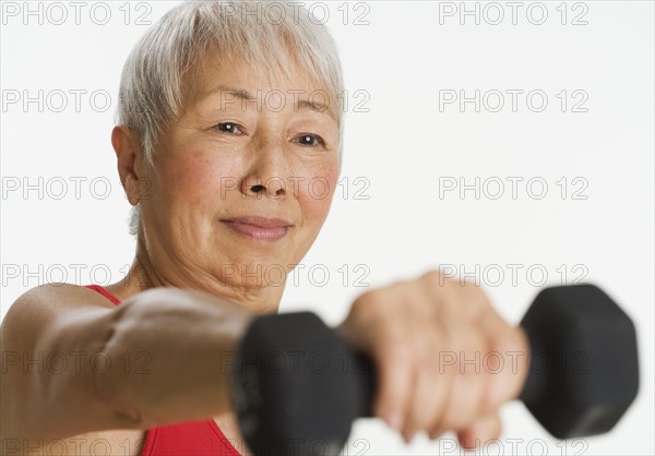 Studio shot of senior Asian woman holding dumbbell