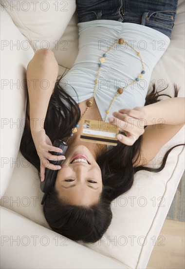 Young Asian woman using telephone and credit card on sofa