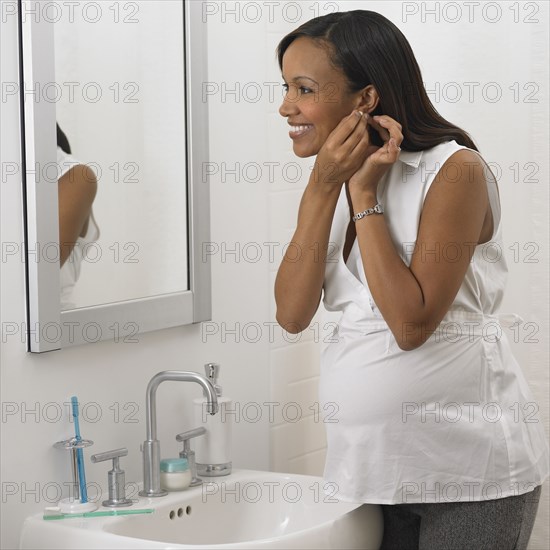 Pregnant African woman putting on earring in bathroom