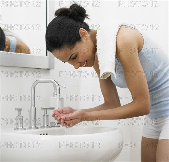 African woman washing face in bathroom sink