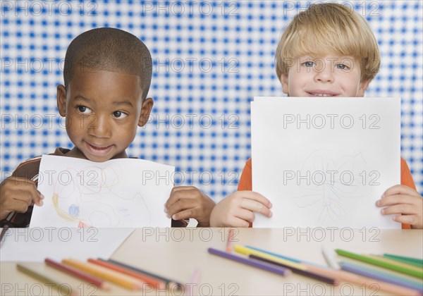 Two young boys holding up drawings