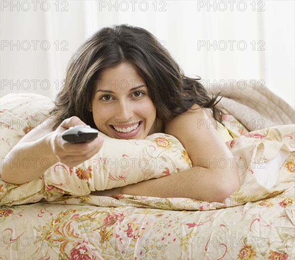 Hispanic woman laying on bed pointing remote control