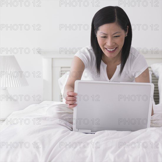 Asian woman using laptop in bed