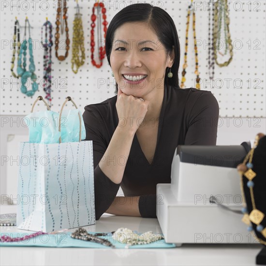 Middle-aged Asian female boutique owner smiling behind counter