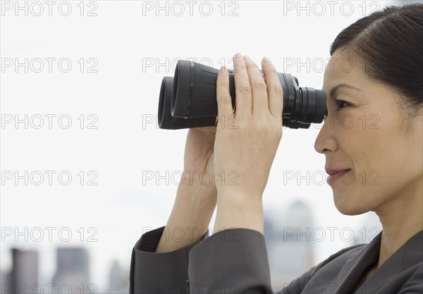 Profile of Asian businesswoman looking through binoculars