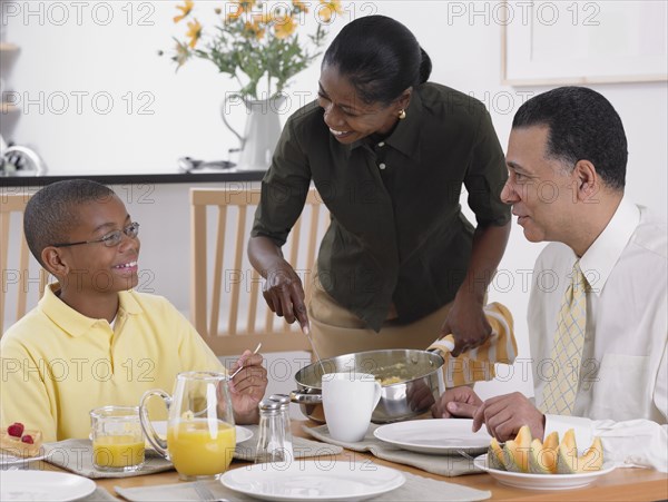 African woman serving breakfast to husband and son