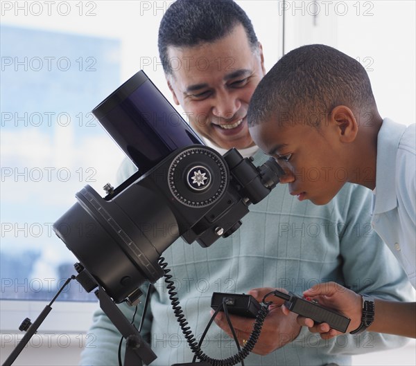 African boy looking into microscope with father