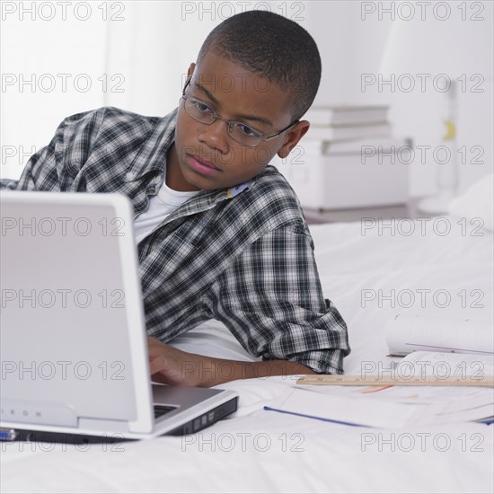 African boy studying with laptop on bed