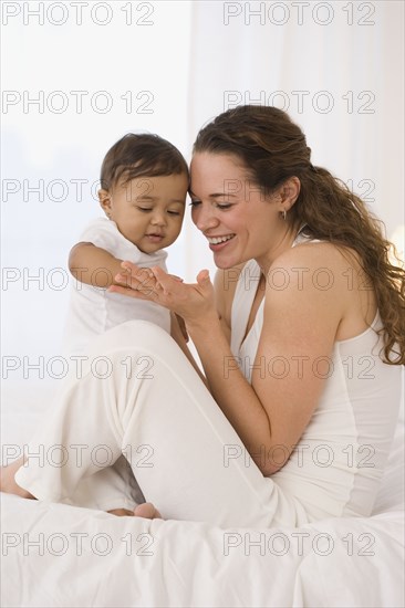 Hispanic mother playing with baby on bed