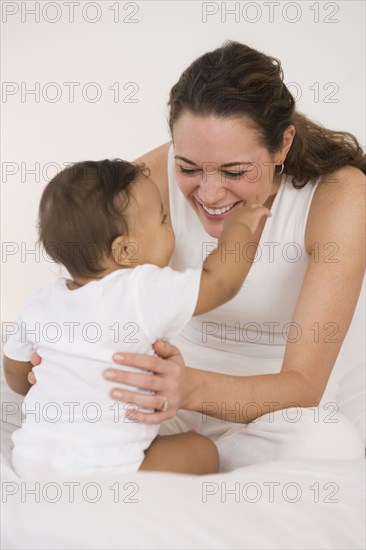 Hispanic mother playing with baby on bed