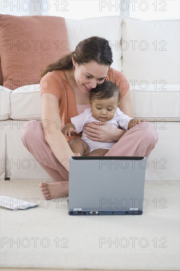 Hispanic mother using laptop with baby in lap