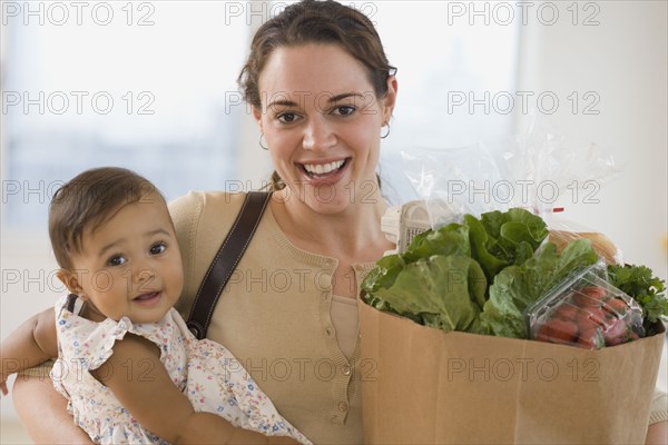 Hispanic mother carrying baby and groceries