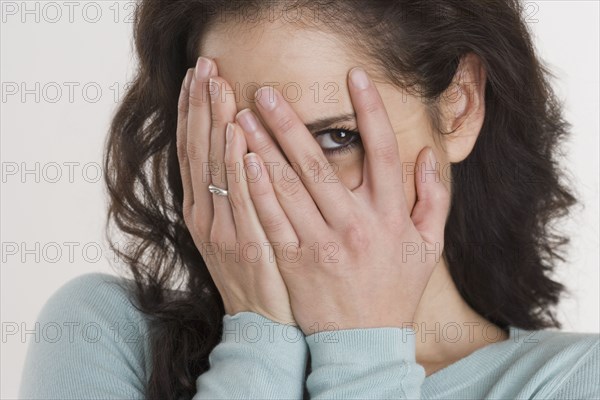 Close up of Hispanic woman peeking through fingers