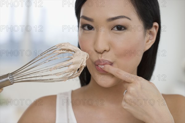 Close up of Asian woman tasting batter on whisk