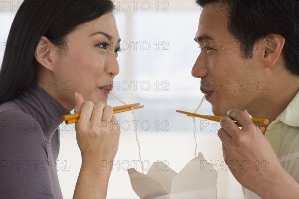 Asian couple eating noodles with chopsticks