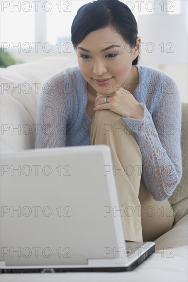 Asian woman using laptop on sofa