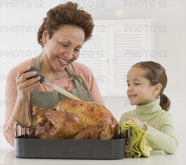 Hispanic grandmother and granddaughter basting roast turkey