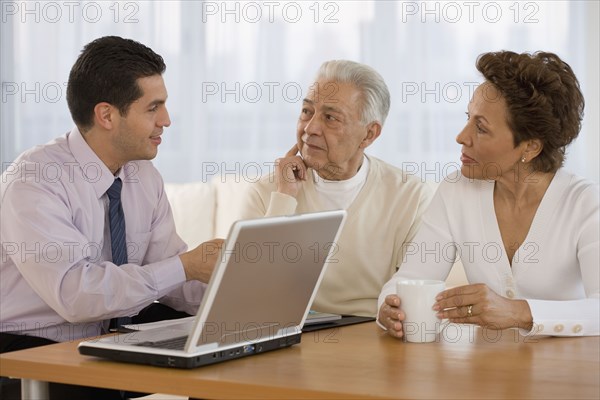 Hispanic businessman talking to senior couple in home