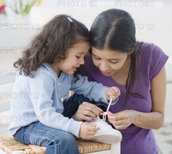 Hispanic mother helping daughter tie shoe