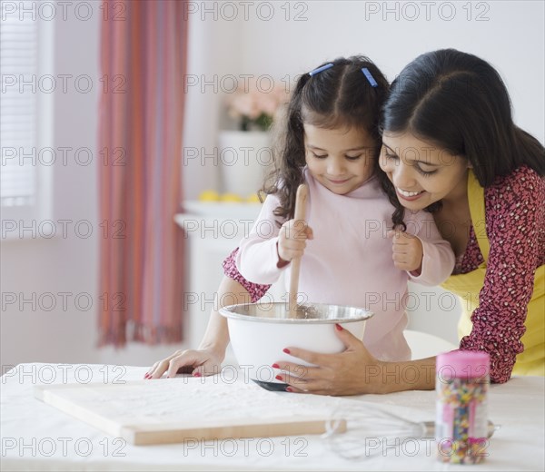 Hispanic mother and daughter mixing batter