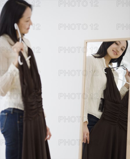Asian woman holding dress up in front of mirror