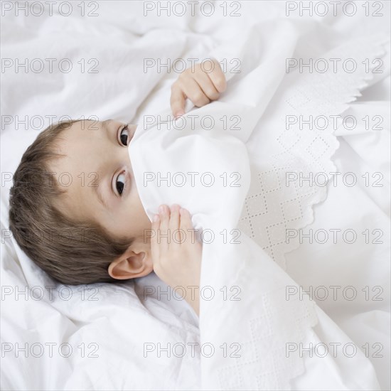 Hispanic boy hiding under covers