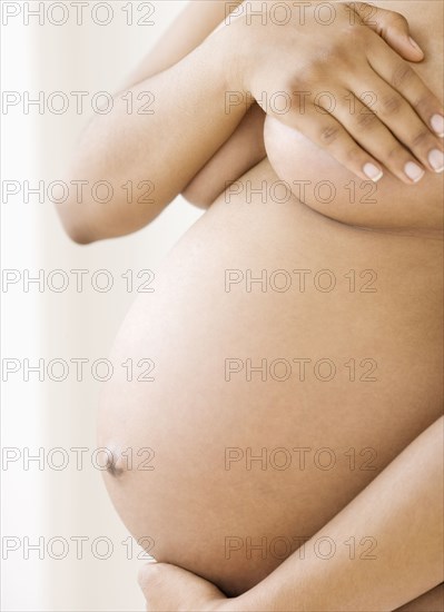 Nude pregnant African American woman covering breasts