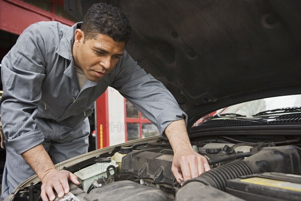 Hispanic male auto mechanic under hood of car