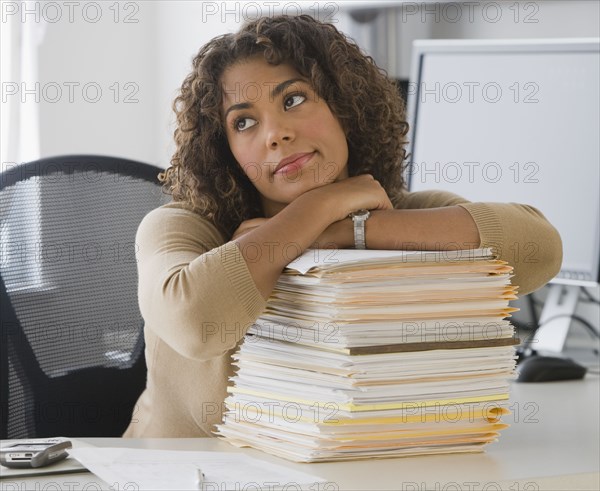 African businesswoman leaning on stack of paperwork