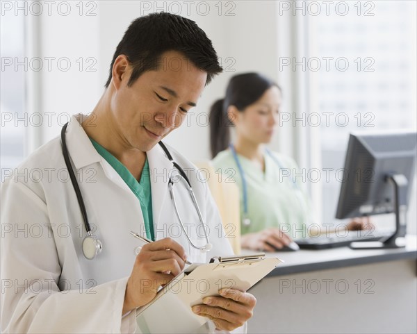 Asian male doctor writing on chart