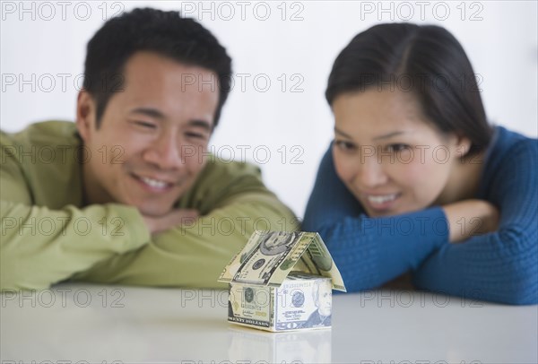 Asian couple looking at house made of money