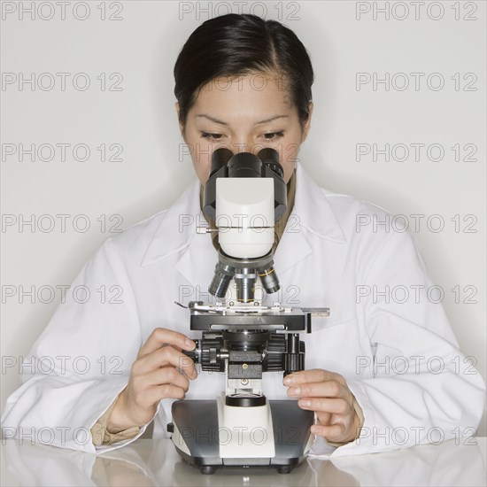 Asian female scientist looking into microscope