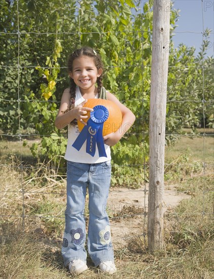 Hispanic girl holding pumpkin with blue ribbon