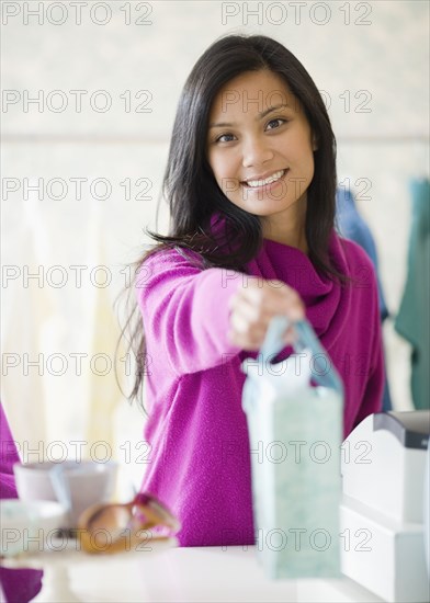 Pacific Islander female sales clerk handing gift bag