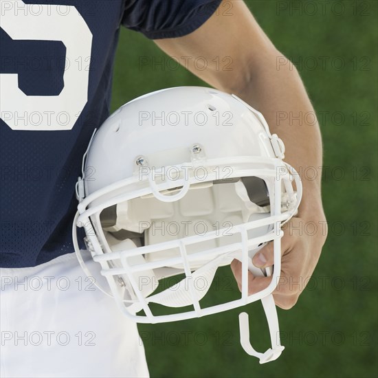 Hispanic male football player holding helmet