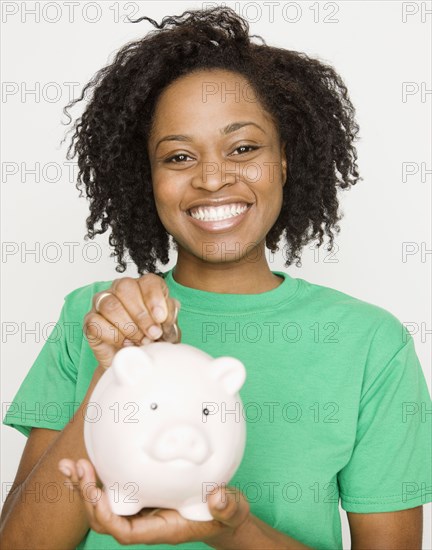 African woman putting coin in piggy bank