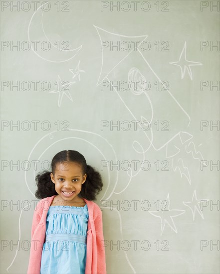 Mixed race girl standing by drawings on blackboard