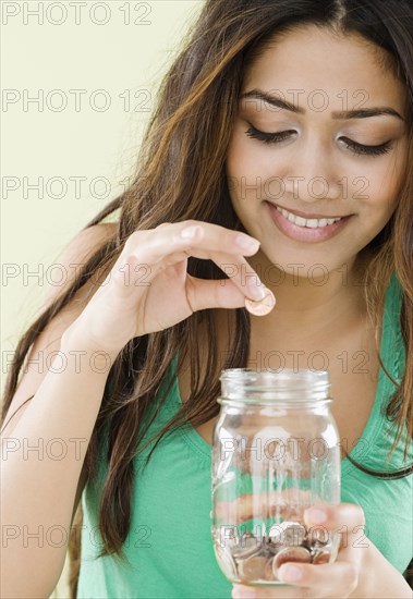 Middle Eastern woman dropping coins in jar