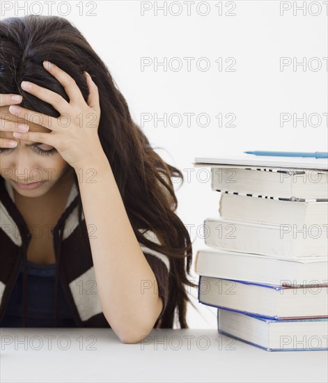 Middle Eastern woman with head in hands next to books