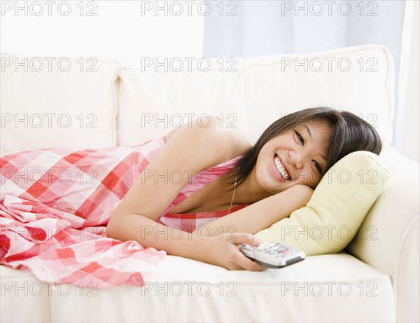 Asian woman laying on sofa watching television